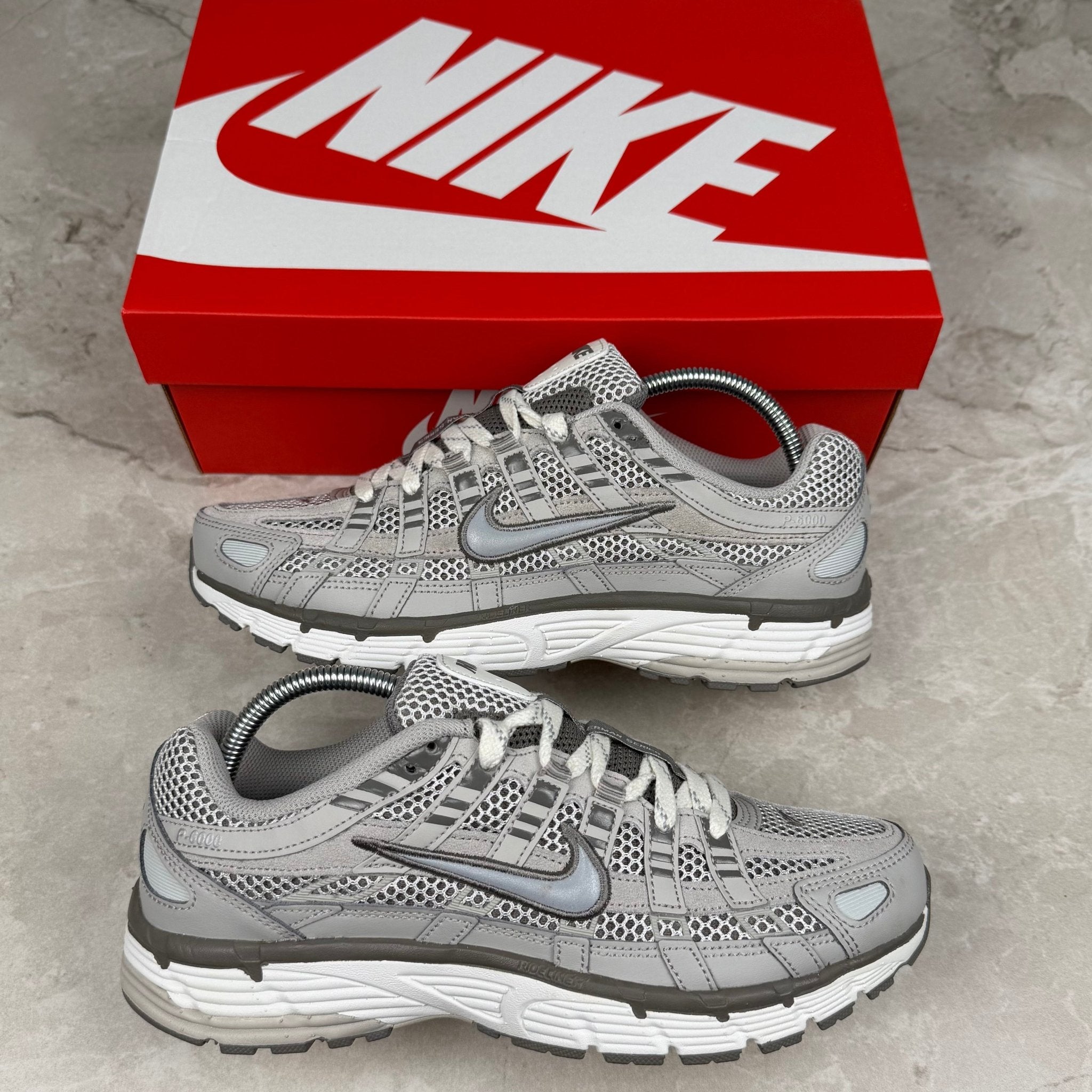 Gray Nike running shoes with a red Nike box on a concrete floor.