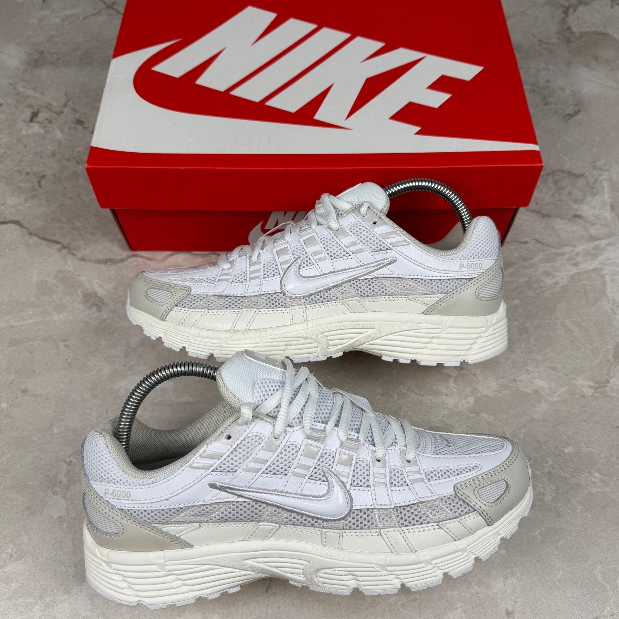 White and gray sneakers with a red Nike box on a concrete floor